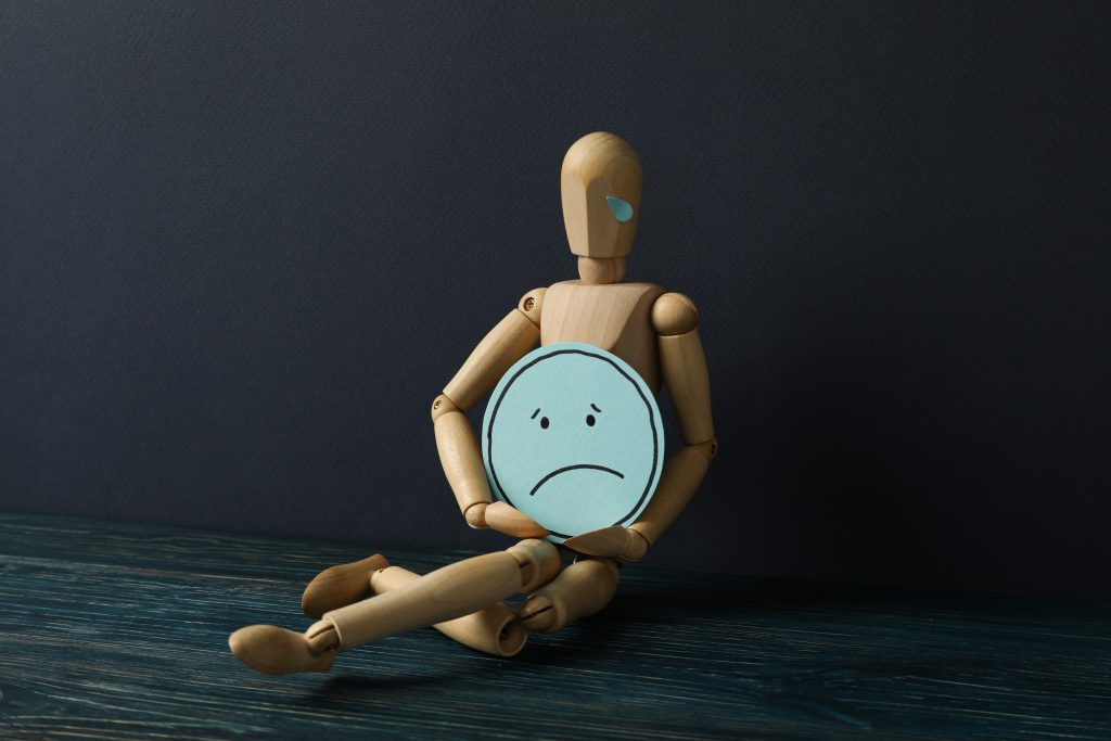 Hands holding a sad face emoji on a dark background